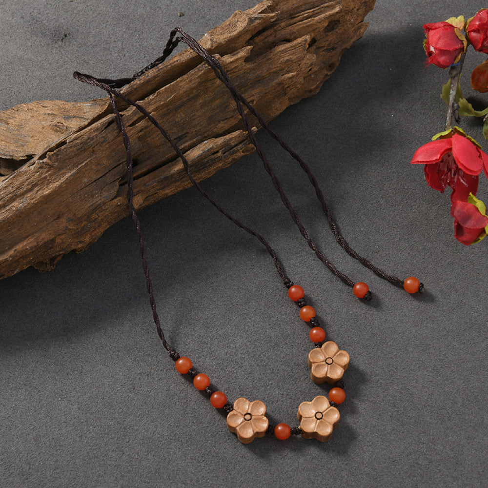 Vintage bohemian ethnic tribal necklace with wooden flower pendants and red beads, featuring a braided rope design, displayed with driftwood and red flowers for a nature-inspired boho look