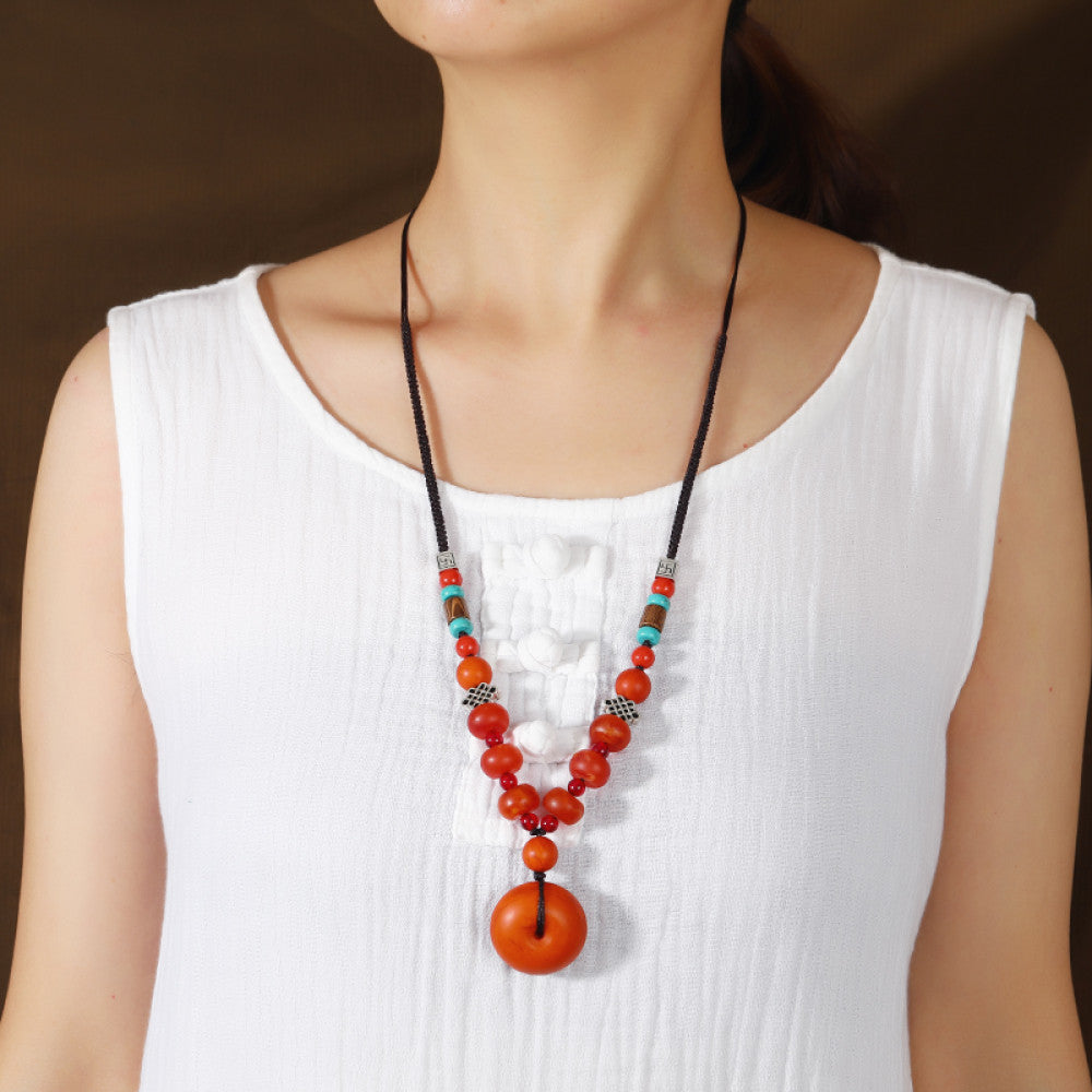 Vintage bohemian ethnic tribal necklace with wooden flower pendants and red beads, featuring a braided rope design, displayed with driftwood and red flowers for a nature-inspired boho look 03