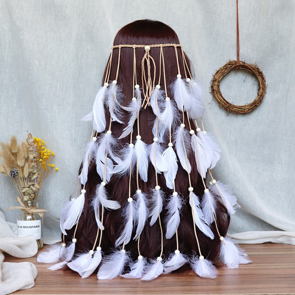 Boho bohemian macramé hair band (worn on long dark brown hair) featuring abundant white feather tassels, wooden bead accents, displayed with dried flower vase & woven wreath decor (against a light fabric background), ideal for bohemian festival fashion styling in the US