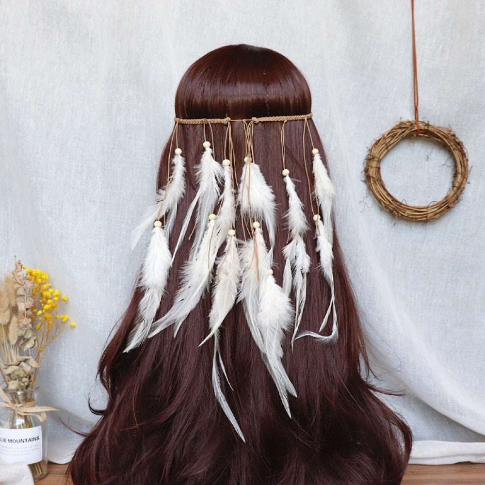 Boho bohemian macramé hair band (worn on long dark brown hair) featuring abundant white feather tassels, wooden bead accents, displayed with dried flower vase & woven wreath decor (against a light fabric background), ideal for bohemian festival fashion styling in the US