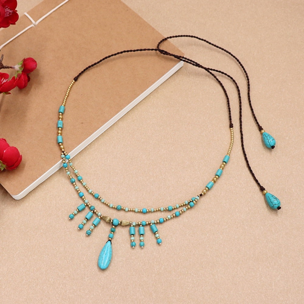 Boho bohemian double-layer choker necklace featuring turquoise beads, tassel pendants, and adjustable black leather cord, displayed on a beige surface