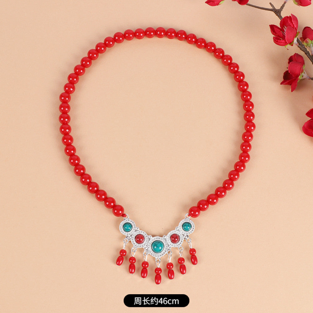 Boho red beaded choker necklace featuring smooth red bead strands, silver-tone decorative centerpiece (with turquoise & red gemstone accents), and red tassel pendants, displayed on a light beige background with red floral decor, ideal for bohemian and traditional fashion enthusiasts in the US