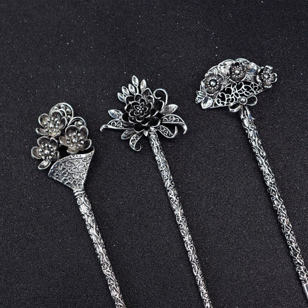 Set of 3 boho vintage ethnic silver-tone hair sticks, each with unique flower decor (cluster, peony, multi-flower) and ornate carved pattern handles, displayed on a black glittery fabric background