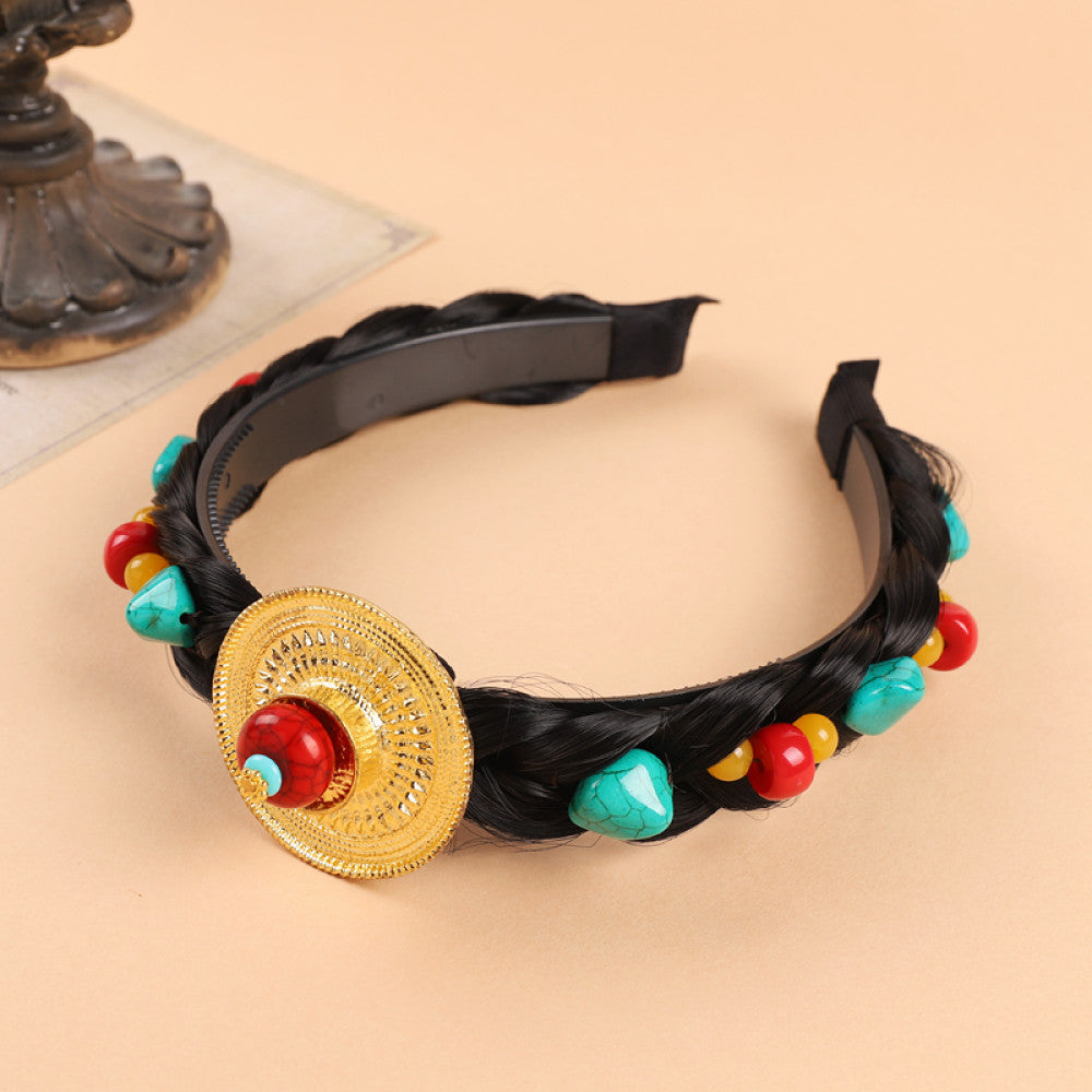 Boho vintage ethnic black braided hair hoop headband (displayed on a soft beige surface with a decorative ornament aside) featuring a prominent gold ornament, plus red, turquoise, and yellow bead details, ideal for bohemian retro ethnic fashion styling in the US