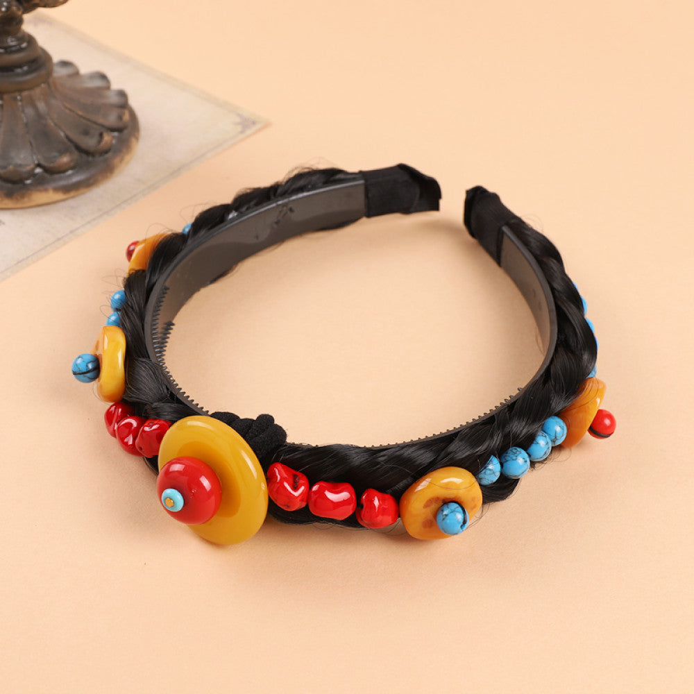 Boho vintage ethnic black braided hair hoop headband (displayed on a soft beige surface with a decorative ornament aside) featuring a prominent gold ornament, plus red, turquoise, and yellow bead details, ideal for bohemian retro ethnic fashion styling in the US 02