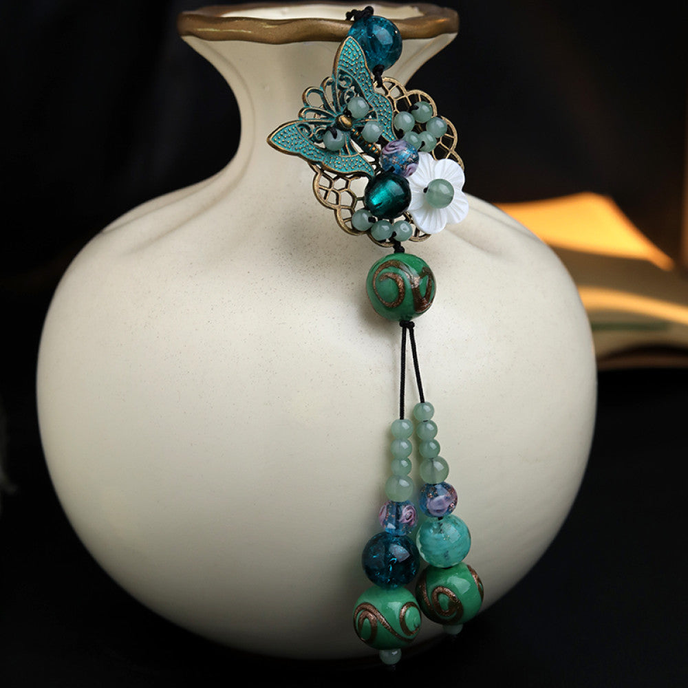 Boho vintage ethnic hair pendant with colorful turquoise/blue beaded tassels, butterfly accent and white flower charm, styled on a black fabric background, ideal for bohemian and traditional fashion enthusiasts in the US 02