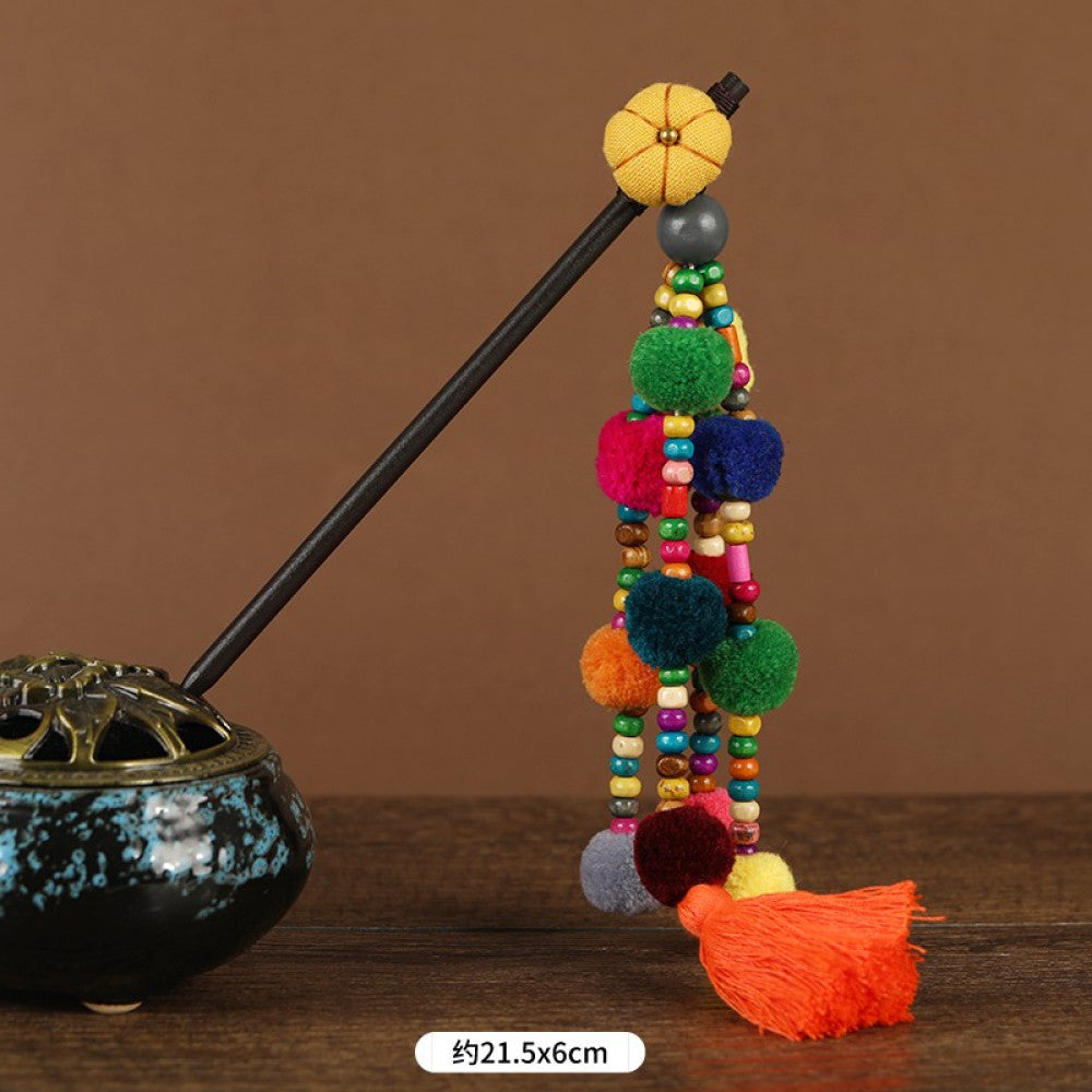 Boho vintage ethnic hair stick pendant featuring colorful pom poms, multi-color beaded accents, and a long orange tassel, displayed alongside an incense burner on a wooden surface against a brown background, ideal for bohemian and traditional fashion enthusiasts in the US