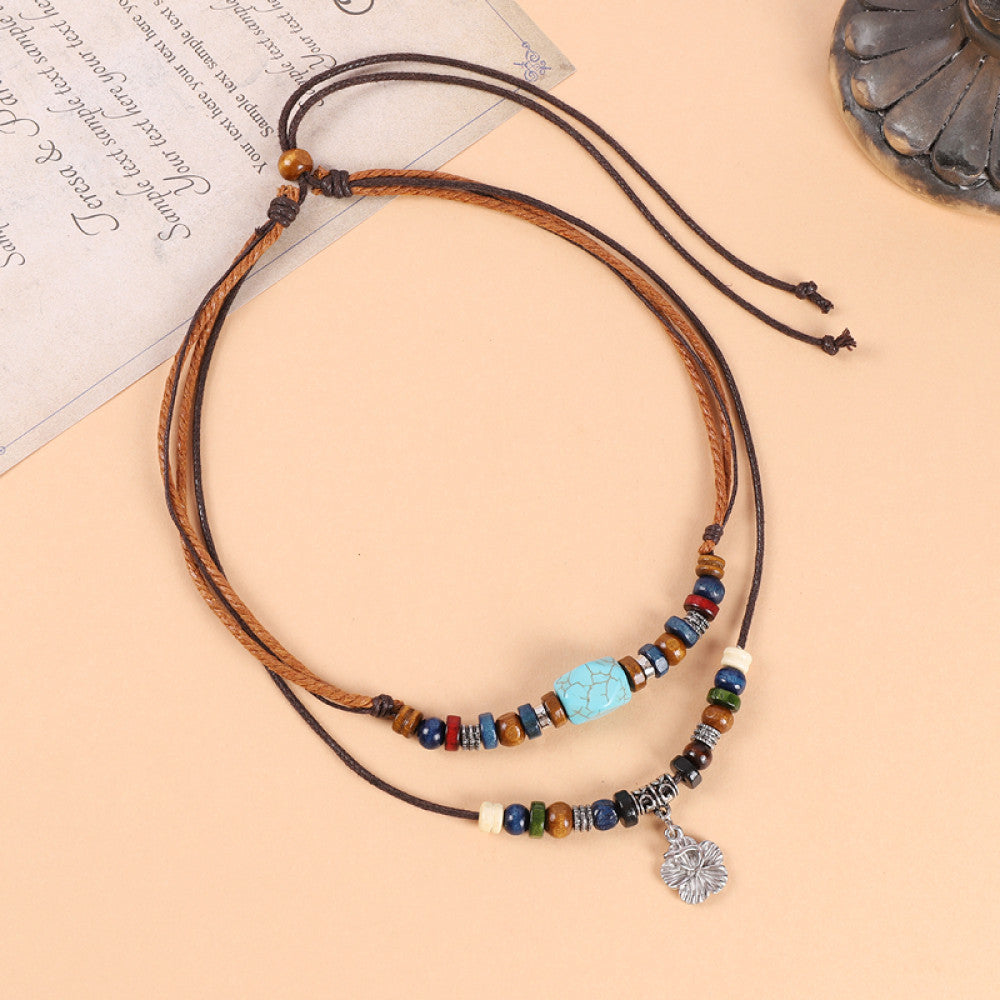 Boho vintage ethnic double-layer leather cord choker necklace (displayed on a soft beige surface alongside a text-printed paper) featuring mixed colorful beads, a turquoise accent piece, and a small decorative pendant, ideal for bohemian casual fashion styling in the US