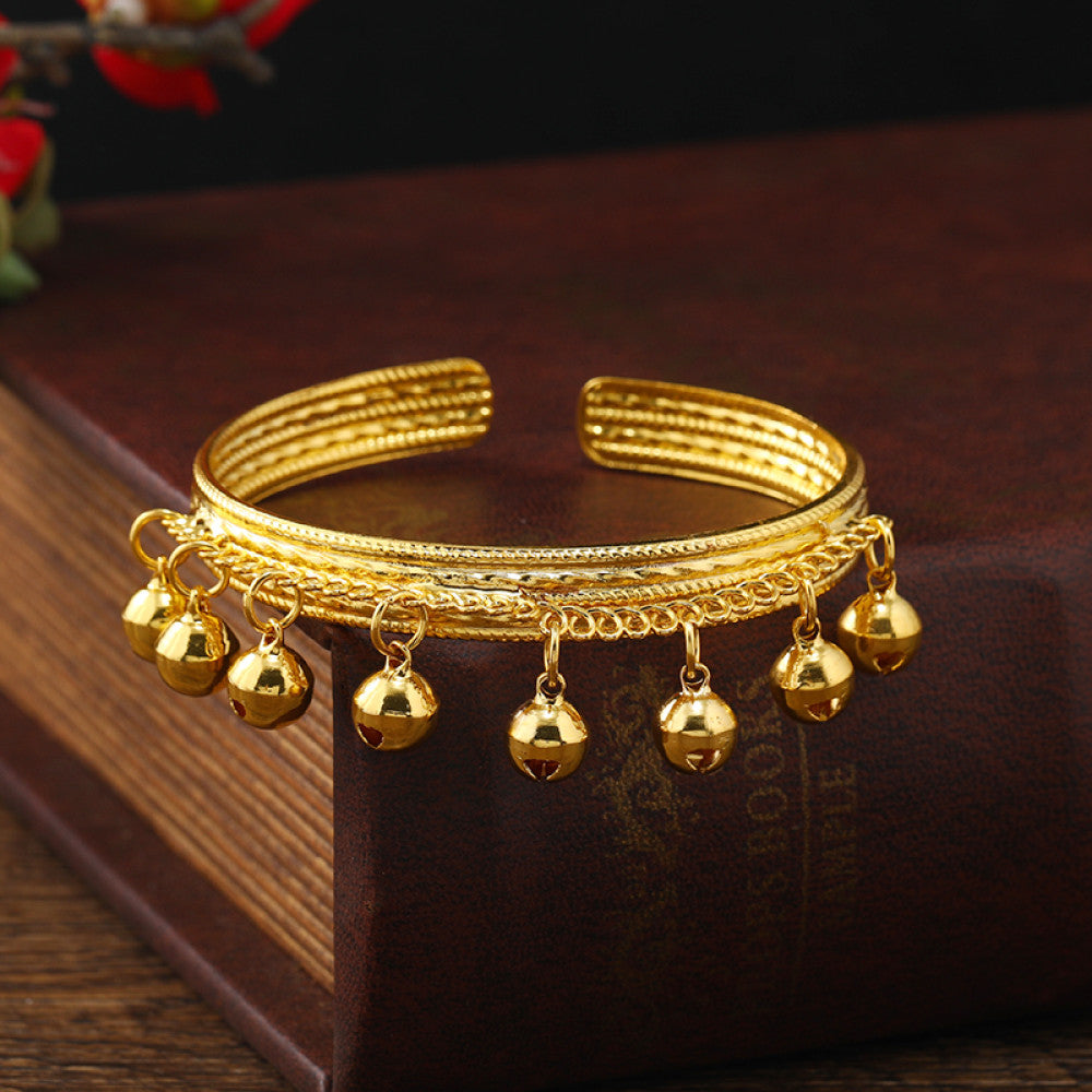 Boho vintage ethnic gold cuff bangle with bell charms, styled on a vintage book, ideal for bohemian and ethnic fashion enthusiasts in the US