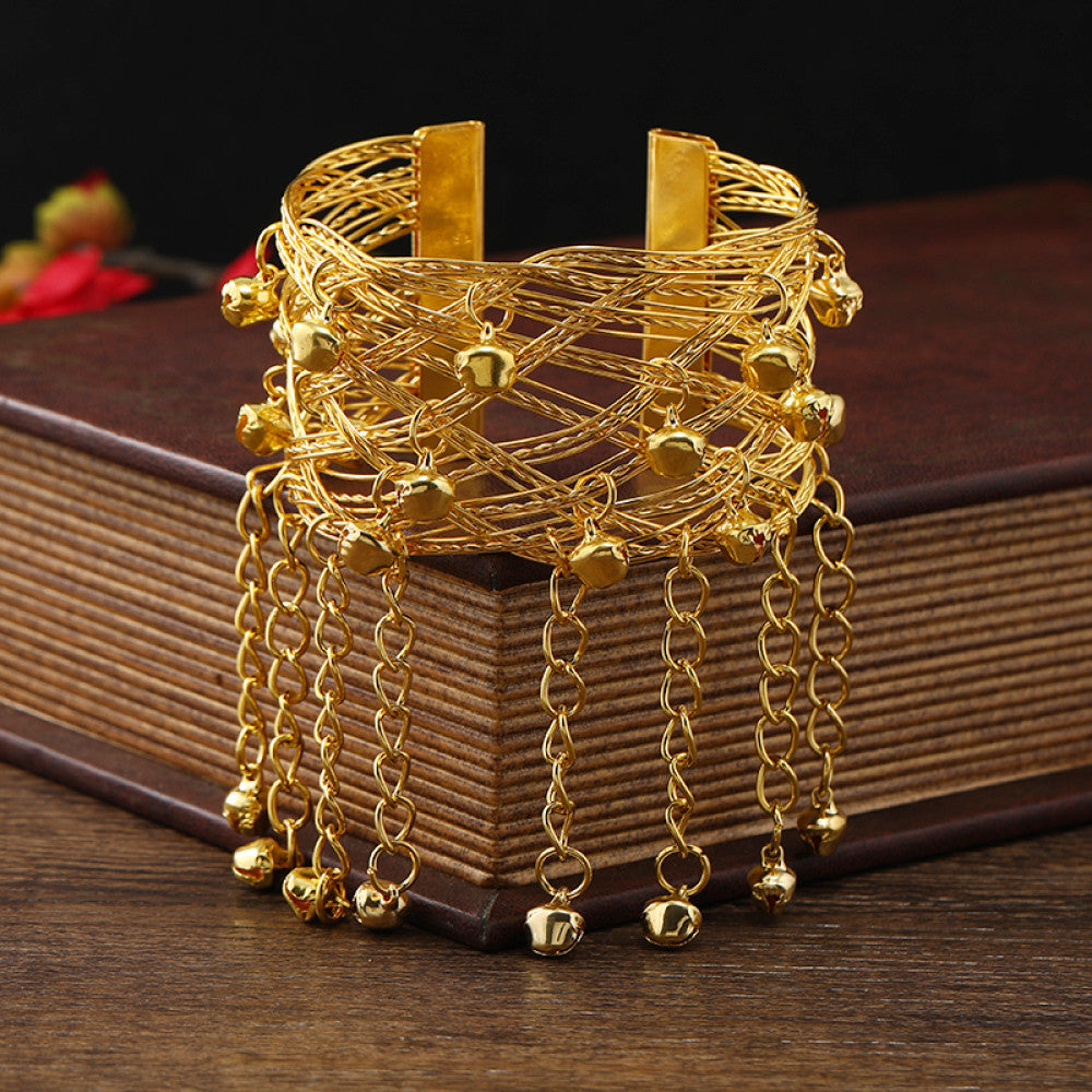 Boho vintage ethnic gold cuff bangle with bell and tassel details, styled on a vintage book, ideal for bohemian and ethnic fashion enthusiasts