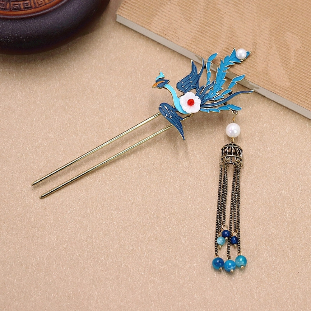 Boho vintage ethnic gold-tone double hair stick featuring a blue phoenix charm (with white flower & red center), pearl accent, birdcage pendant, and blue/white beaded tassels, displayed alongside a ceramic vessel on a warm brown background, ideal for bohemian and traditional fashion enthusiasts in the US 02