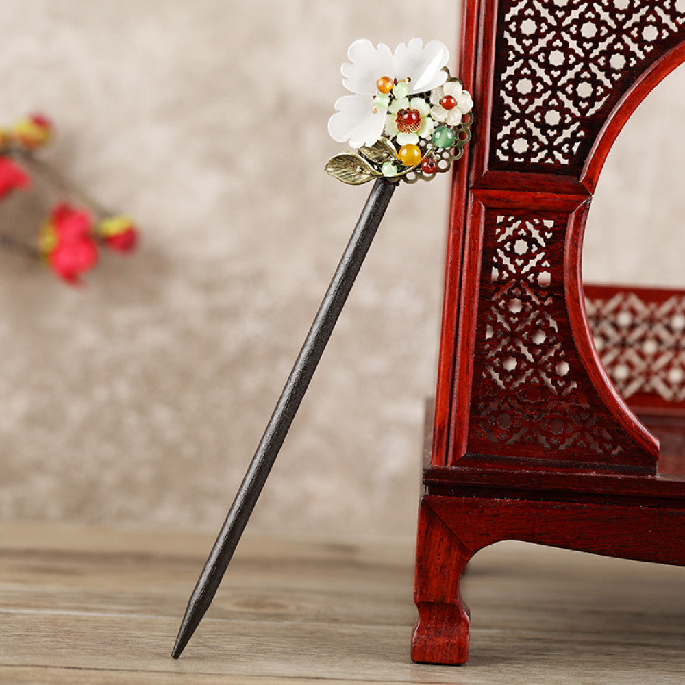 Boho vintage ethnic hair stick featuring a dark wooden-look handle, topped with light green flower, red bead, and green leaf decorative accents, displayed beside a red carved wooden decor 03