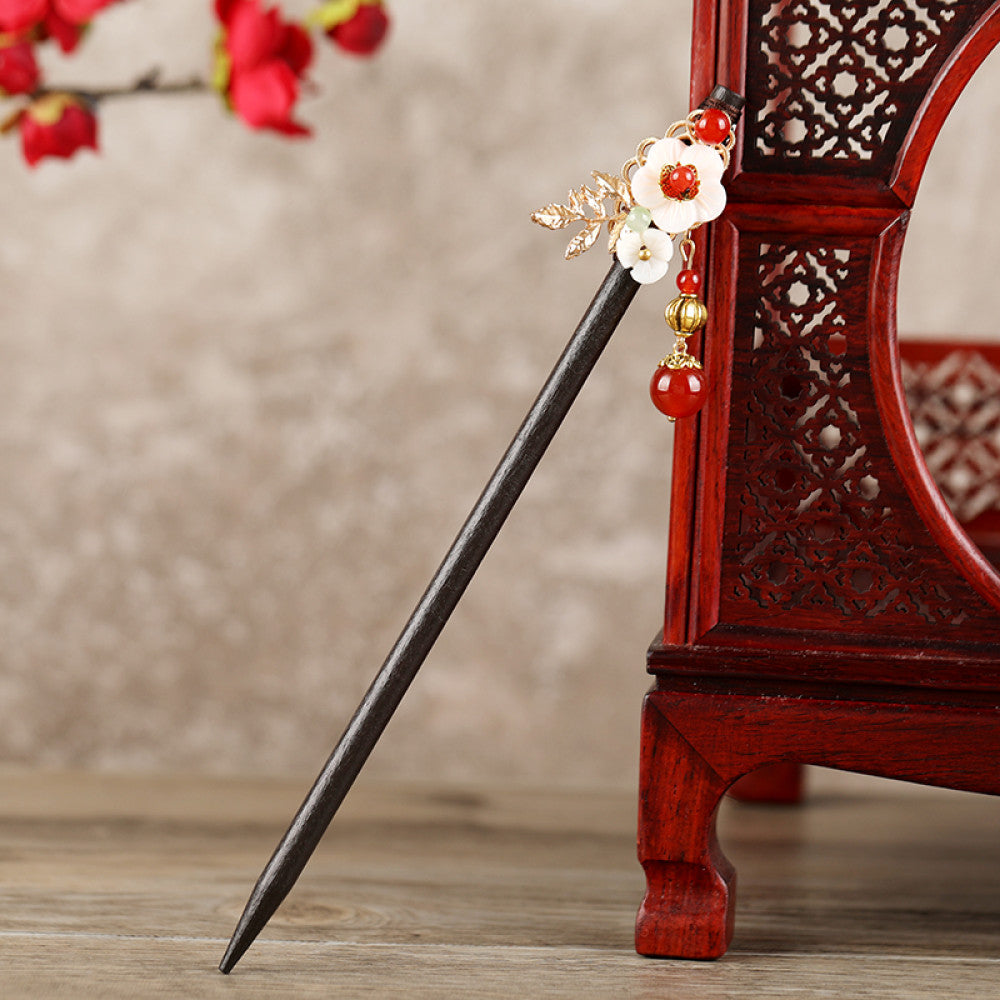 Boho vintage ethnic hair stick featuring a dark wooden-look handle, topped with light green flower, red bead, and green leaf decorative accents, displayed beside a red carved wooden decor  05