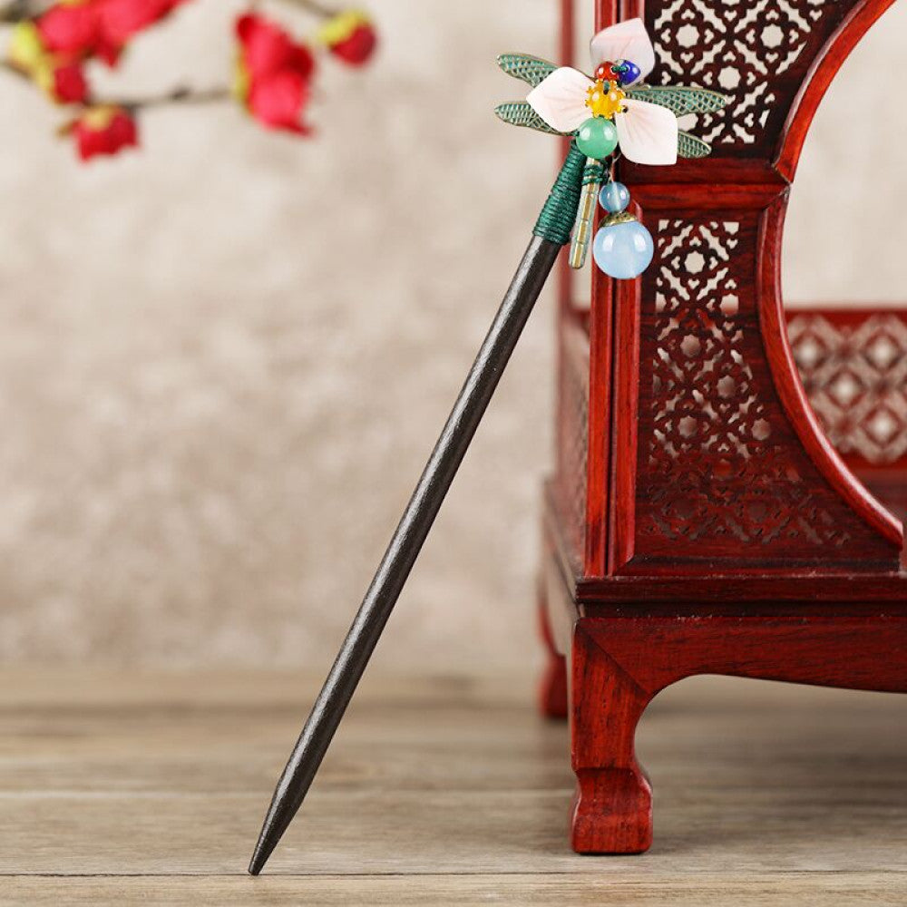 Boho vintage ethnic hair stick featuring a dark wooden-look handle, topped with light green flower, red bead, and green leaf decorative accents, displayed beside a red carved wooden decor  06
