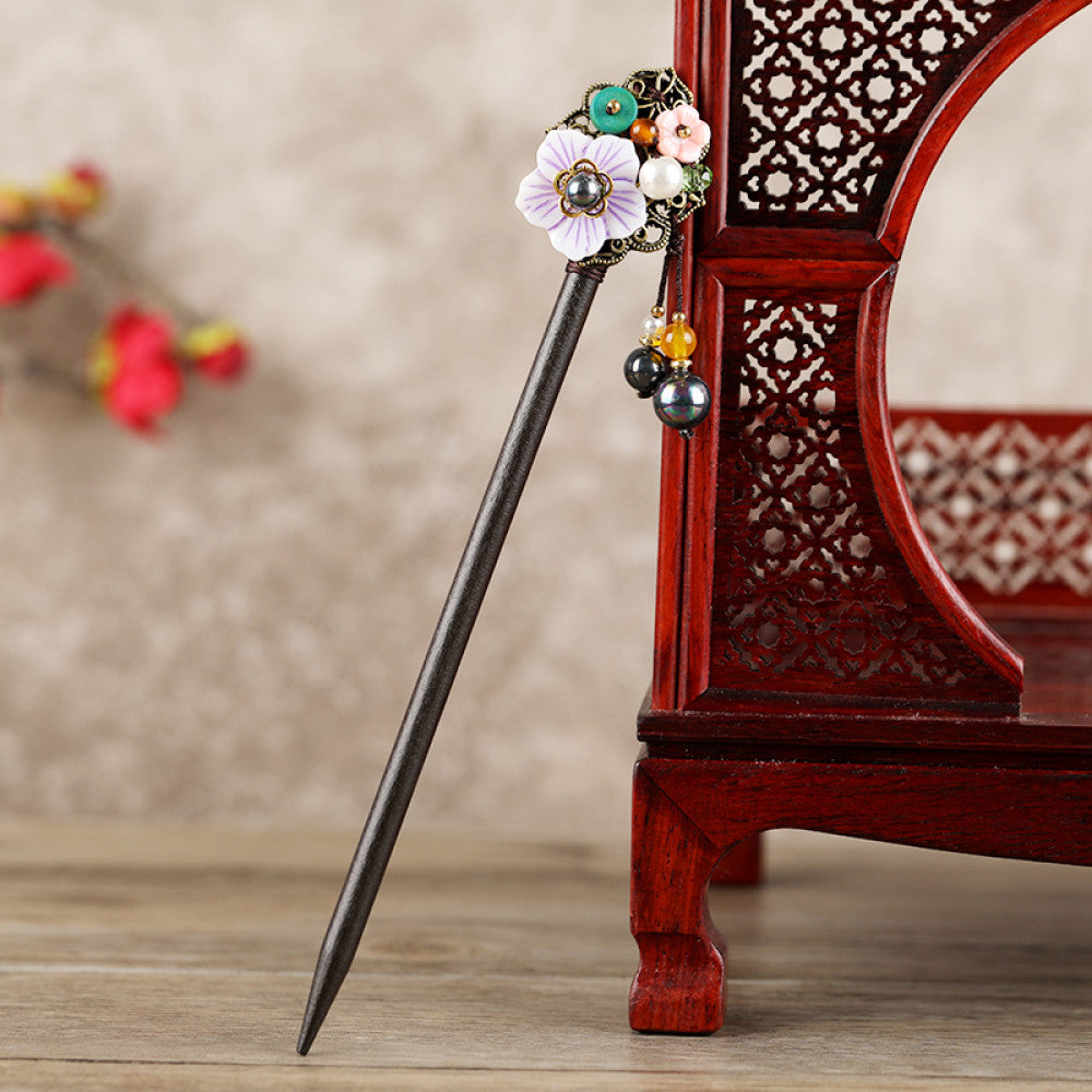 Boho vintage ethnic hair stick featuring a dark wooden-look handle, topped with light green flower, red bead, and green leaf decorative accents, displayed beside a red carved wooden decor , ideal for bohemian and traditional fashion enthusiasts in the US 02
