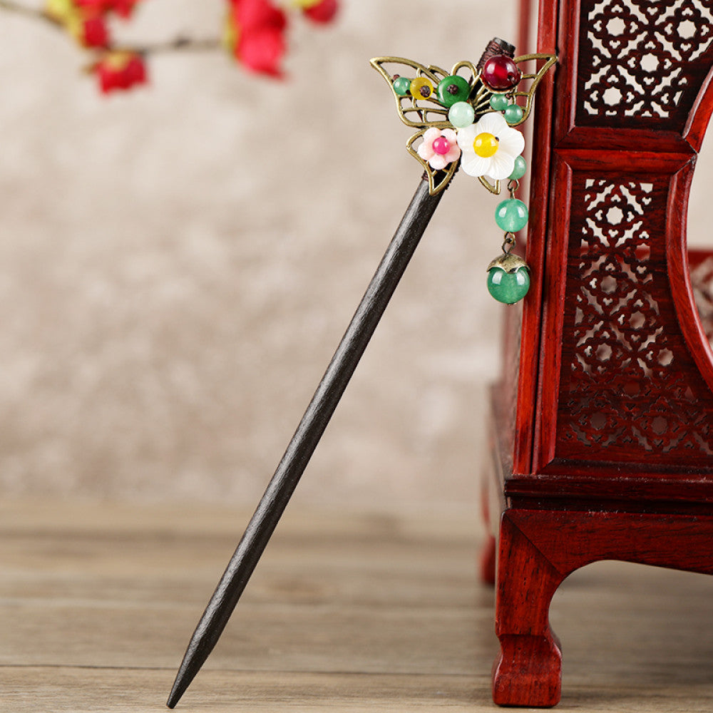 Boho vintage ethnic hair stick featuring a dark wooden-look handle, topped with light green flower, red bead, and green leaf decorative accents, displayed beside a red carved wooden decor , ideal for bohemian and traditional fashion enthusiasts in the US 05