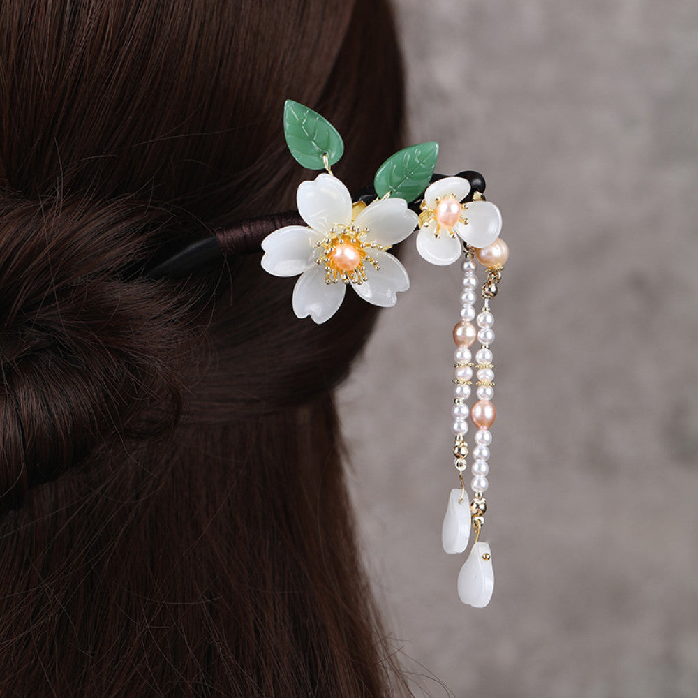 Boho vintage ethnic hair stick ornament (clipped in dark styled hair) featuring a pink flower (red center), green leaf accents, pink/green bead tassel, and light green leaf pendant, displayed against a muted gray background, ideal for bohemian traditional fashion styling in the US 01