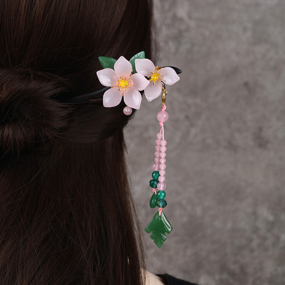 Boho vintage ethnic hair stick ornament (clipped in dark styled hair) featuring a pink flower (red center), green leaf accents, pink/green bead tassel, and light green leaf pendant, displayed against a muted gray background, ideal for bohemian traditional fashion styling in the US 02