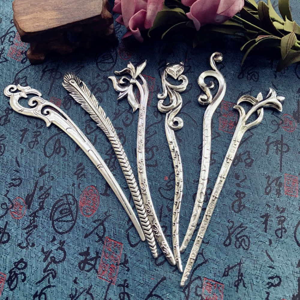 et of 5 boho vintage ethnic silver-tone hair sticks, featuring assorted decor (feather, flower, curved patterns & braided details), displayed on a blue fabric with text patterns (alongside a wooden box & pink roses), ideal for bohemian and traditional fashion enthusiasts in the US