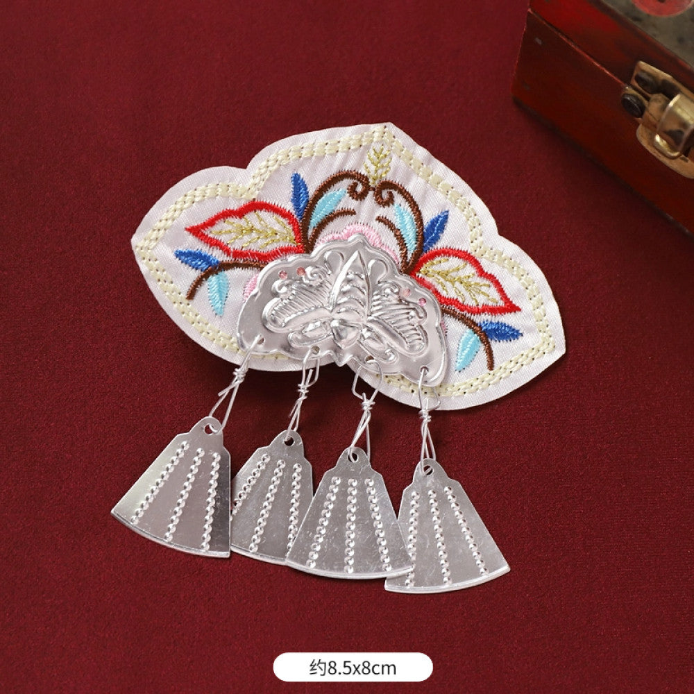 Boho vintage ethnic silver-tone decorative brooch featuring an intricate butterfly charm, pink floral embroidered accent (with blue details), and bell tassel pendants, displayed on a red fabric background  03