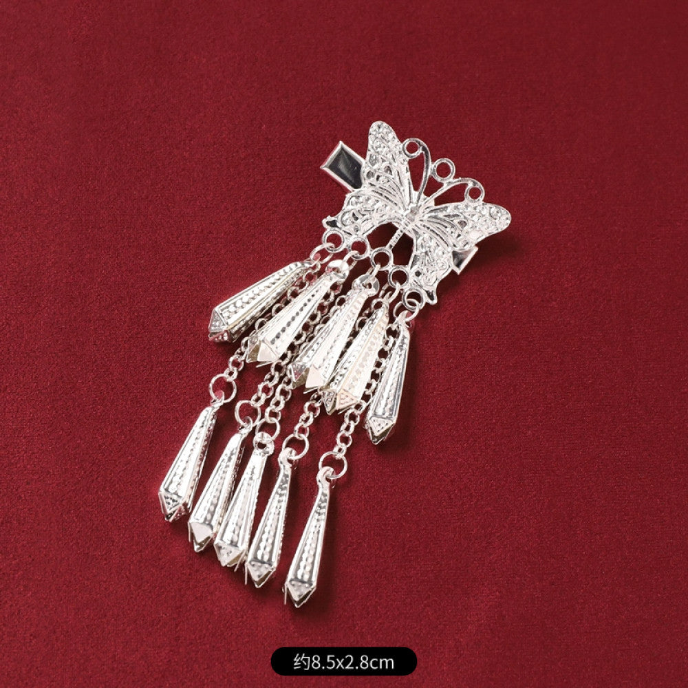 Boho vintage ethnic silver-tone decorative pendant featuring an intricate round patterned center, multiple silver-tone fish charms, and layered bell tassel fringe, displayed on a rich red fabric background