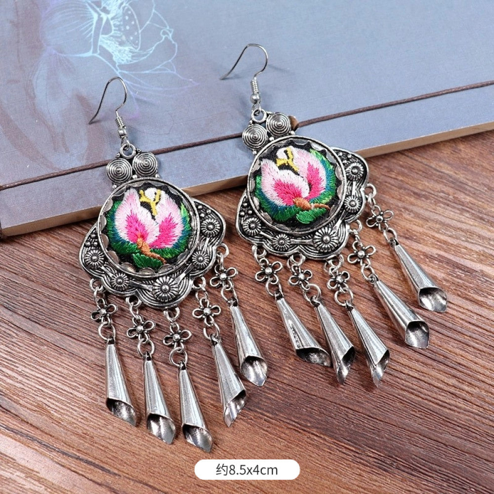 Boho vintage ethnic silver-tone earrings set (displayed on a wooden surface with a patterned notebook background) featuring embroidered lotus details and layered silver bell fringe pendants, ideal for bohemian retro or traditional fashion styling in the US