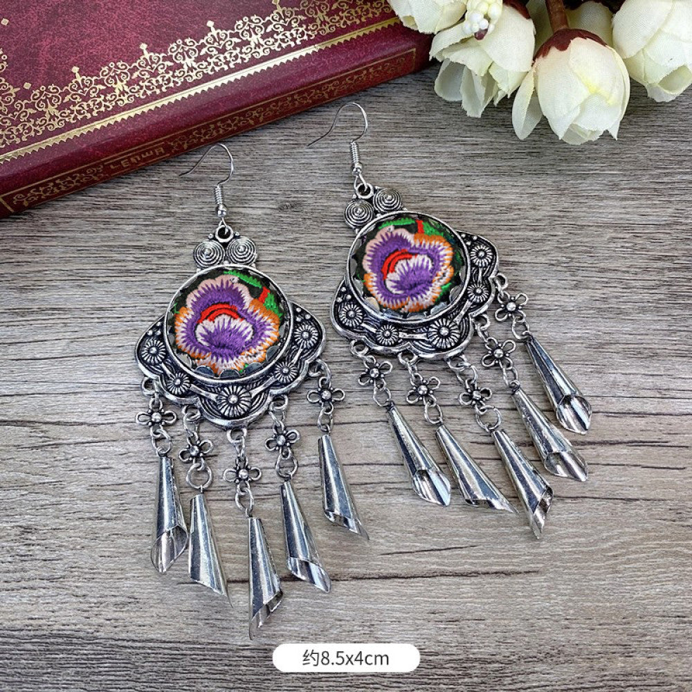 Boho vintage ethnic silver-tone earrings set (displayed on a wooden surface with a patterned notebook background) featuring embroidered lotus details and layered silver bell fringe pendants, ideal for bohemian retro or traditional fashion styling in the US 01