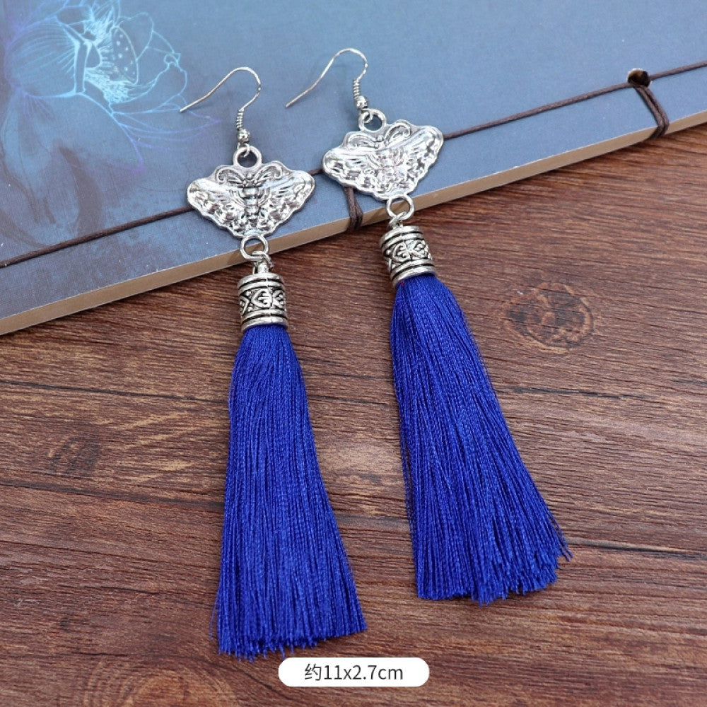 Boho vintage ethnic silver-tone earrings set (displayed on a wooden surface with a patterned notebook background) featuring embroidered lotus details and layered silver bell fringe pendants, ideal for bohemian retro or traditional fashion styling in the US 03