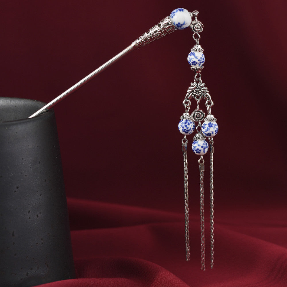 Boho vintage ethnic silver-tone hair stick featuring blue-and-white porcelain-style beads, intricate decorative details, and layered chain tassel fringe, displayed with a black vessel on a rich red fabric background, ideal for bohemian and traditional fashion enthusiasts in the US 01