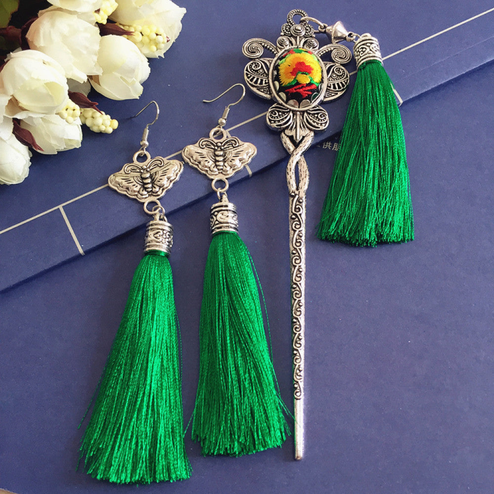 Boho vintage ethnic silver-tone hair stick & earring set (displayed on a blue background alongside white flowers) featuring ornate details, a colorful accent (on the hair stick), butterfly design (on earrings), and lush green tassels, ideal for bohemian retro or traditional fashion styling in the US