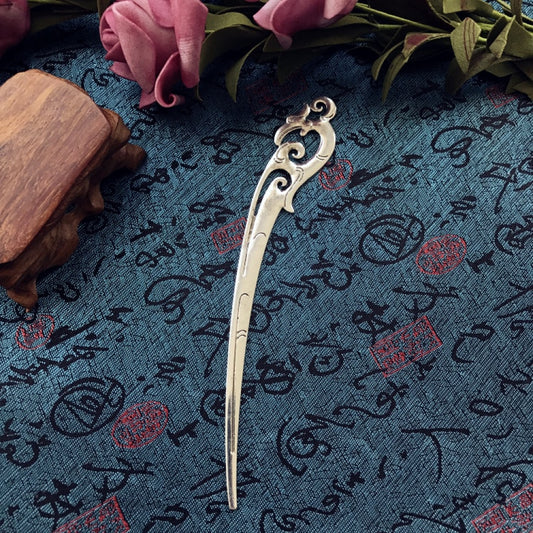 
Boho vintage ethnic silver-tone hair stick featuring an intricate curved decorative top, displayed on a blue fabric with text patterns