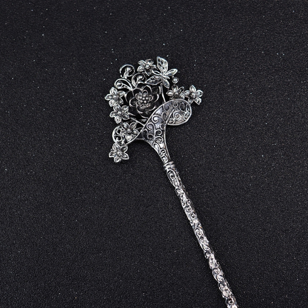 Boho vintage ethnic silver tone hair stick featuring a detailed flower cluster top and ornate carved pattern handle, displayed on a black glittery fabric background 01