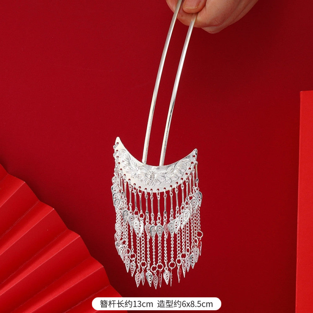 Boho vintage ethnic silver-tone hair stick (hand-held display against a rich red background alongside a red folding fan) featuring intricate openwork details and layered tassel fringe, ideal for bohemian retro or traditional Hanfu fashion styling in the US