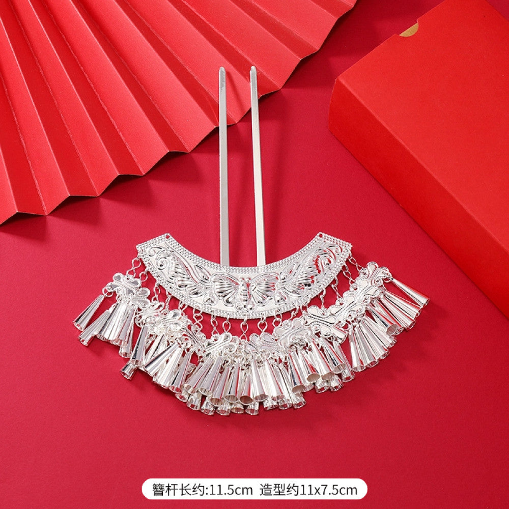 Boho vintage ethnic silver-tone hair stick (hand-held display against a rich red background alongside a red folding fan) featuring intricate openwork details and layered tassel fringe, ideal for bohemian retro or traditional Hanfu fashion styling in the US 05