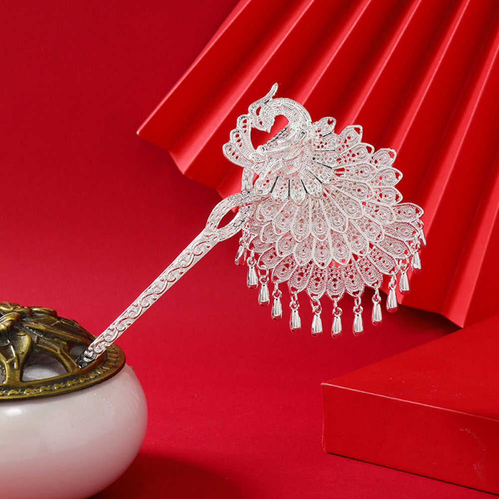Boho vintage ethnic silver-tone hair stick (displayed with a white vessel & red decorative backdrop) featuring an elaborate peacock openwork design and layered bell tassel fringe, ideal for bohemian traditional fashion styling in the US