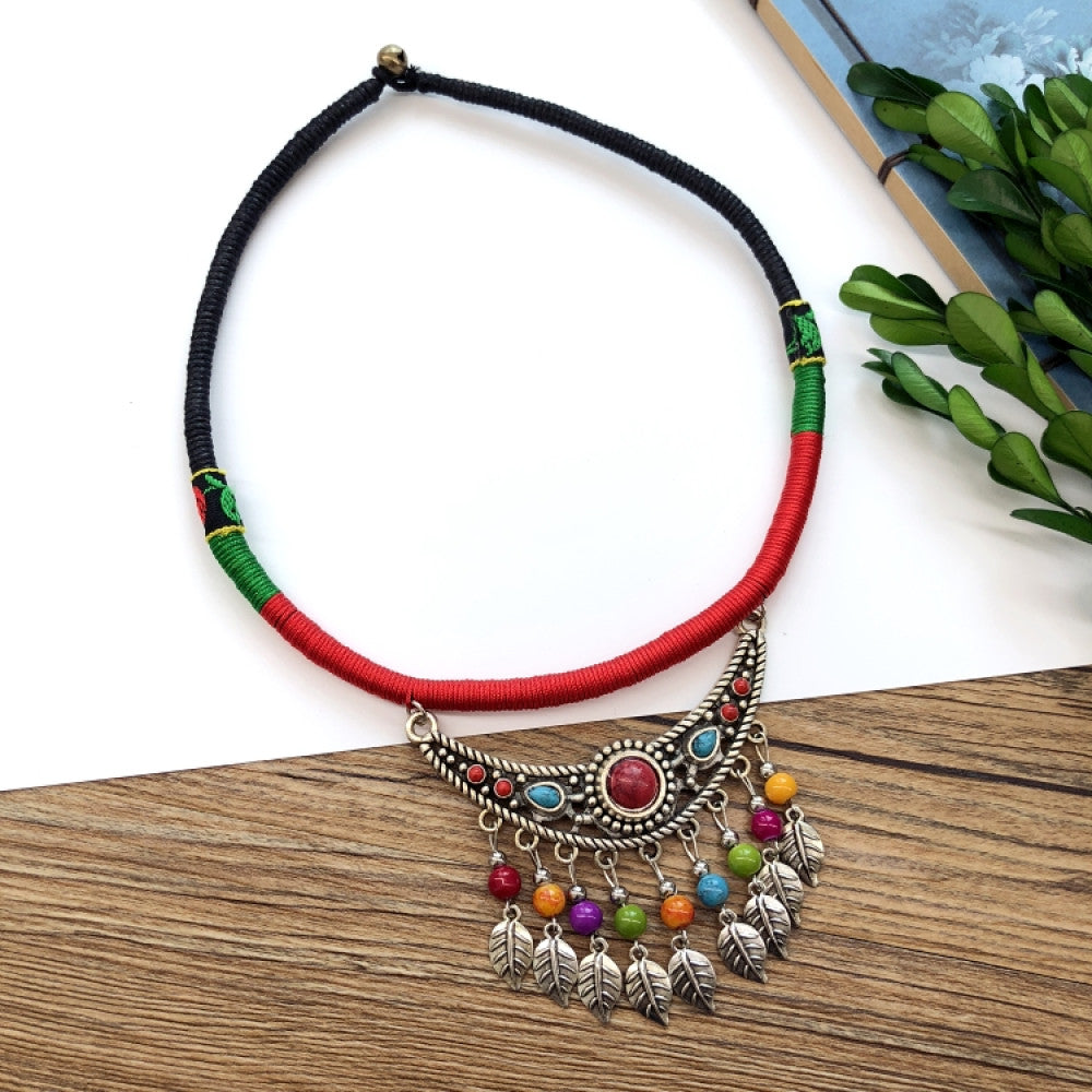 Boho vintage ethnic tri-color (black/red/green) rope choker necklace, featuring a silver-tone ornate fringe pendant with colorful bead details, displayed on a wooden surface (paired with white background, green foliage & a notebook), ideal for bohemian casual fashion styling in the US 01