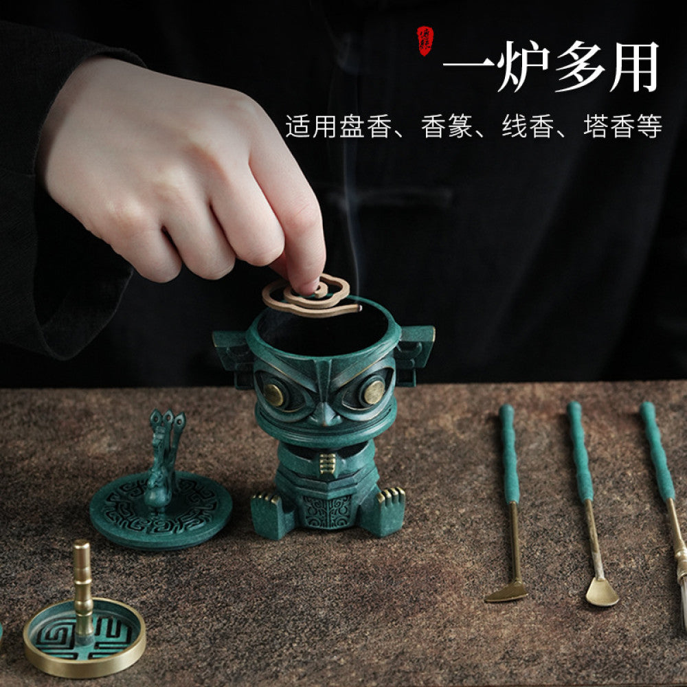 A bronze-style incense burner displayed with matching incense tools on a dark background.