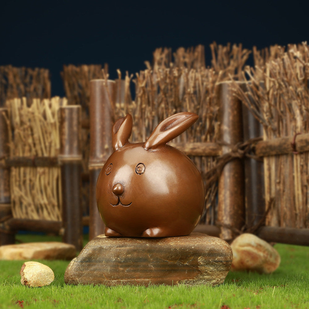 Charming bronze bunny statue with a rounded design, set against a rustic bamboo fence backdrop, a Feng Shui symbol of good fortune, ideal as whimsical home decor