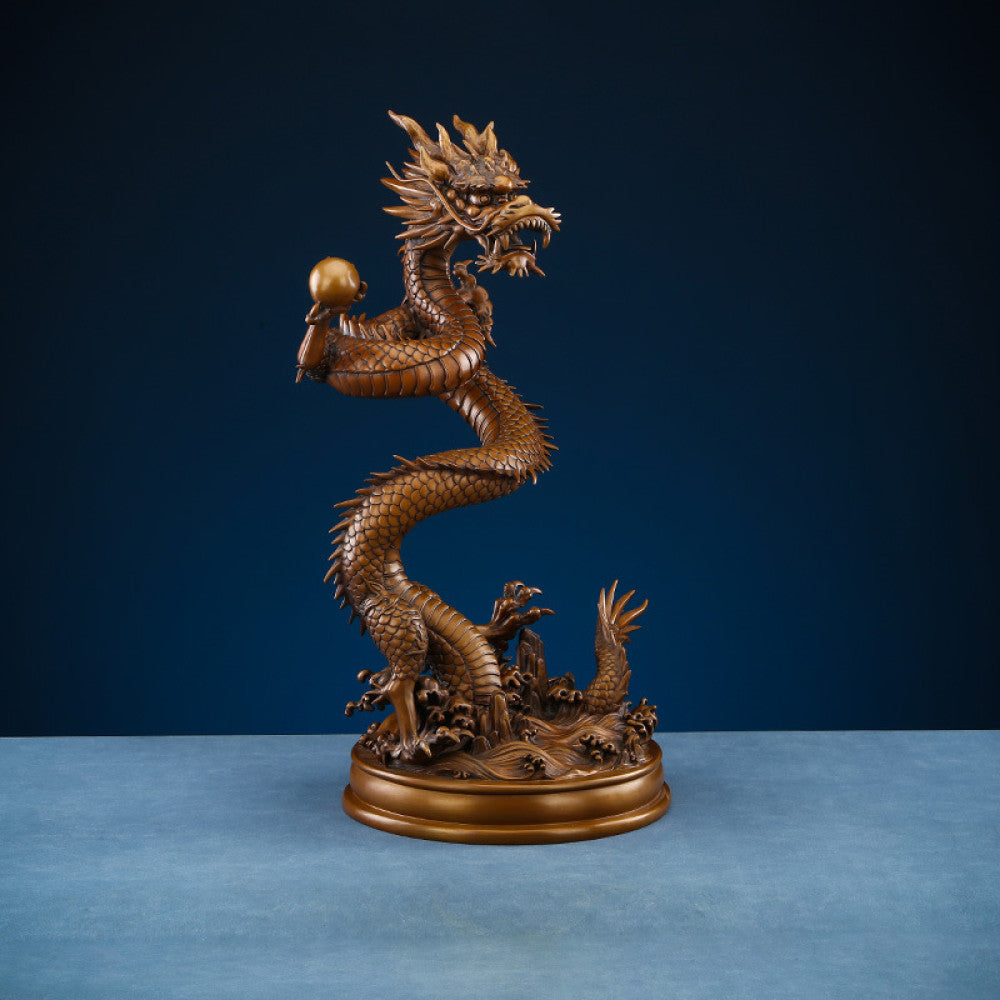 Intricate bronze Chinese dragon statue coiled around a pearl, a symbol of power and good fortune in Feng Shui, displayed on a blue surface against a dark blue background 02