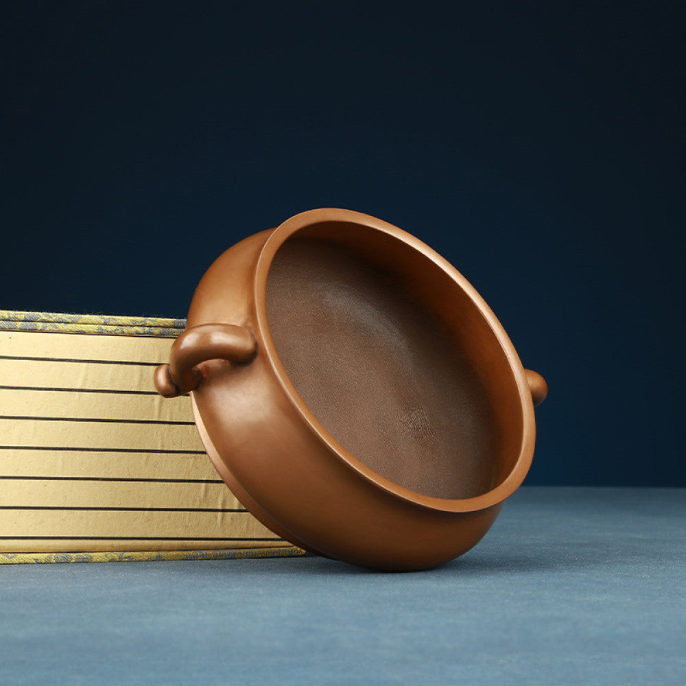 Polished bronze Chinese incense burner with elegant ruyi-shaped handles and a rounded body, a Feng Shui symbol of wealth and harmony, displayed as refined home decor against a dark blue backdrop on a textured surface 04