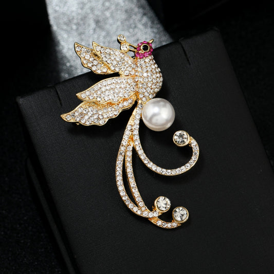 This elegant brooch features a sparkling crystal-encrusted bird in a gold-tone setting, accented by a lustrous pearl and delicate pink detail at its head. A sophisticated statement piece for any outfit