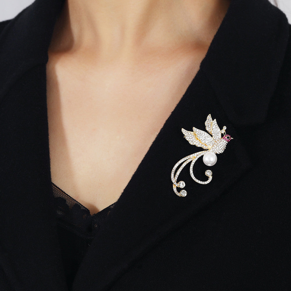This elegant brooch features a sparkling crystal-encrusted bird in a gold-tone setting, accented by a lustrous pearl and delicate pink detail at its head. A sophisticated statement piece for any outfit 03