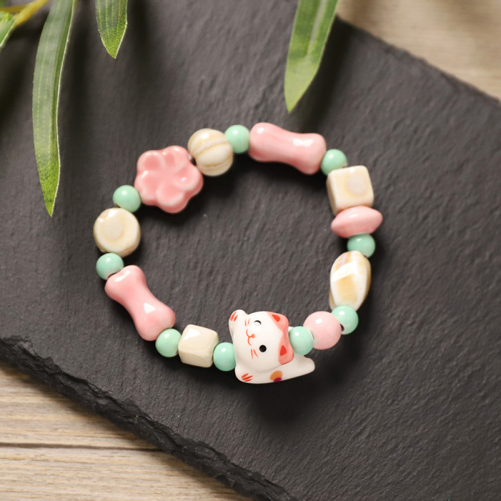 This playful beaded bracelet features a charming lucky cat ceramic bead at its center, paired with whimsical ceramic charms like stars, bones, and flowers, interspersed with small brown beads. Crafted from ceramic, it brings a cute, kawaii vibe to everyday outfits 01