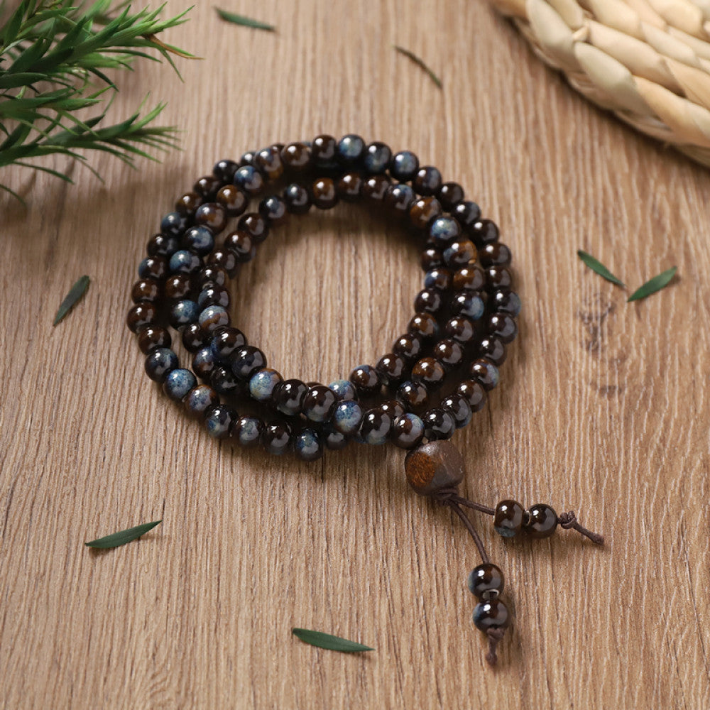 Deep brown patterned beads, textured and antique, with small tassel pendant.