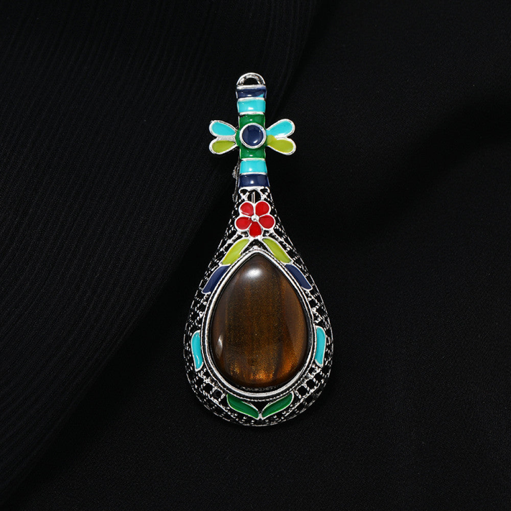 This exquisite brooch features a unique musical instrument-inspired design, crafted with intricate filigree metalwork and vibrant enamel accents. A large, warm amber-hued gemstone takes center stage, surrounded by colorful enamel details that add playful charm. The antiqued silver-tone base enhances its vintage appeal, making it a standout accessory for blazers, scarves, or special occasion outfits, blending artistic craftsmanship with timeless elegance.
