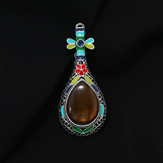 This exquisite brooch features a unique musical instrument-inspired design, crafted with intricate filigree metalwork and vibrant enamel accents. A large, warm amber-hued gemstone takes center stage, surrounded by colorful enamel details that add playful charm. The antiqued silver-tone base enhances its vintage appeal, making it a standout accessory for blazers, scarves, or special occasion outfits, blending artistic craftsmanship with timeless elegance.