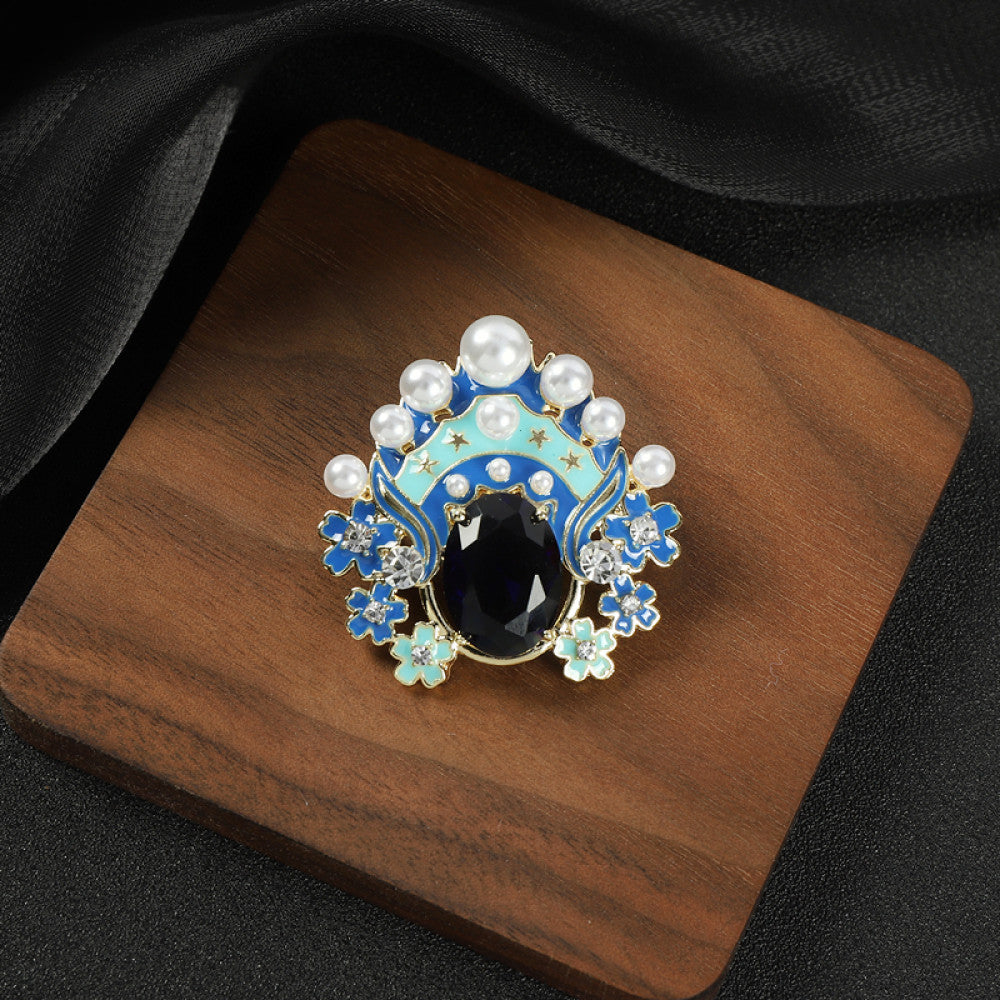 This striking brooch features a bold, theatrical-inspired design with vibrant enamel, lustrous pearls, and a prominent red crystal at its center. Delicate floral motifs and sparkling crystals add intricate detail, making it a standout accessory for blazers, scarves, or dresses. Perfect for adding a pop of color and artistic flair to any outfit, this piece is sure to make a memorable statement. 01