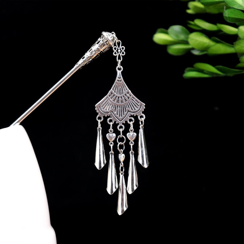 silver-tone hair stick featuring turquoise beads, an intricate round decorative element, and layered chain tassel fringe, displayed beside a white vessel green foliage 01