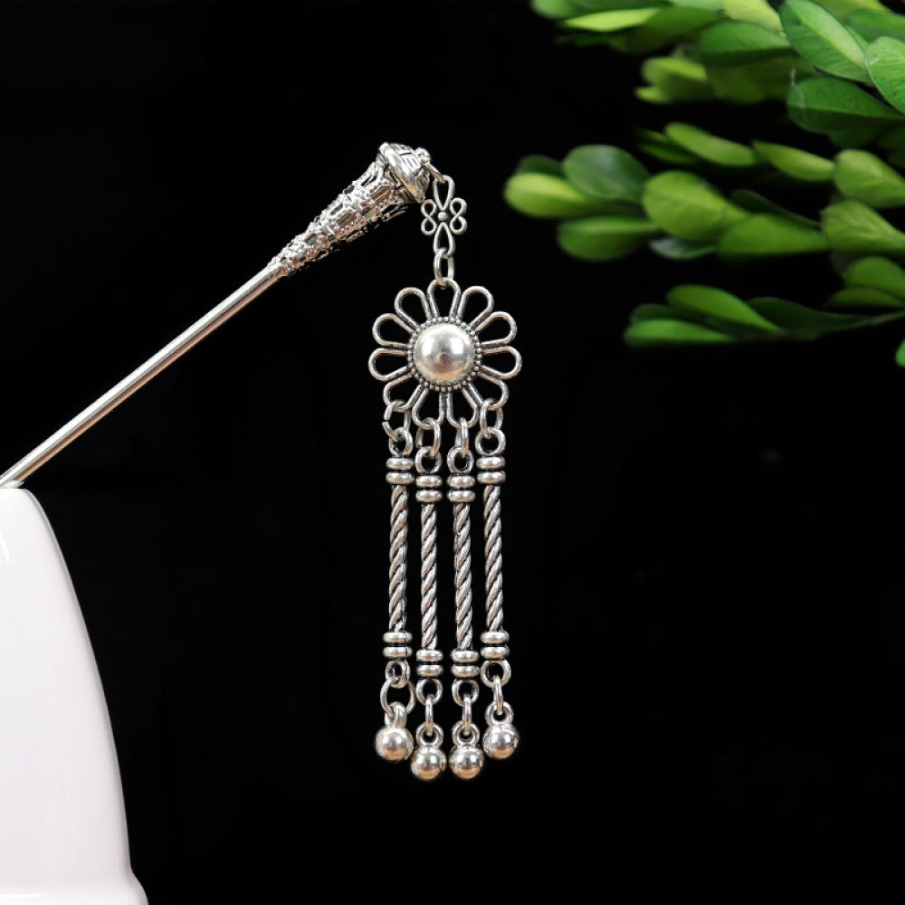 silver-tone hair stick featuring turquoise beads, an intricate round decorative element, and layered chain tassel fringe, displayed beside a white vessel green foliage 03