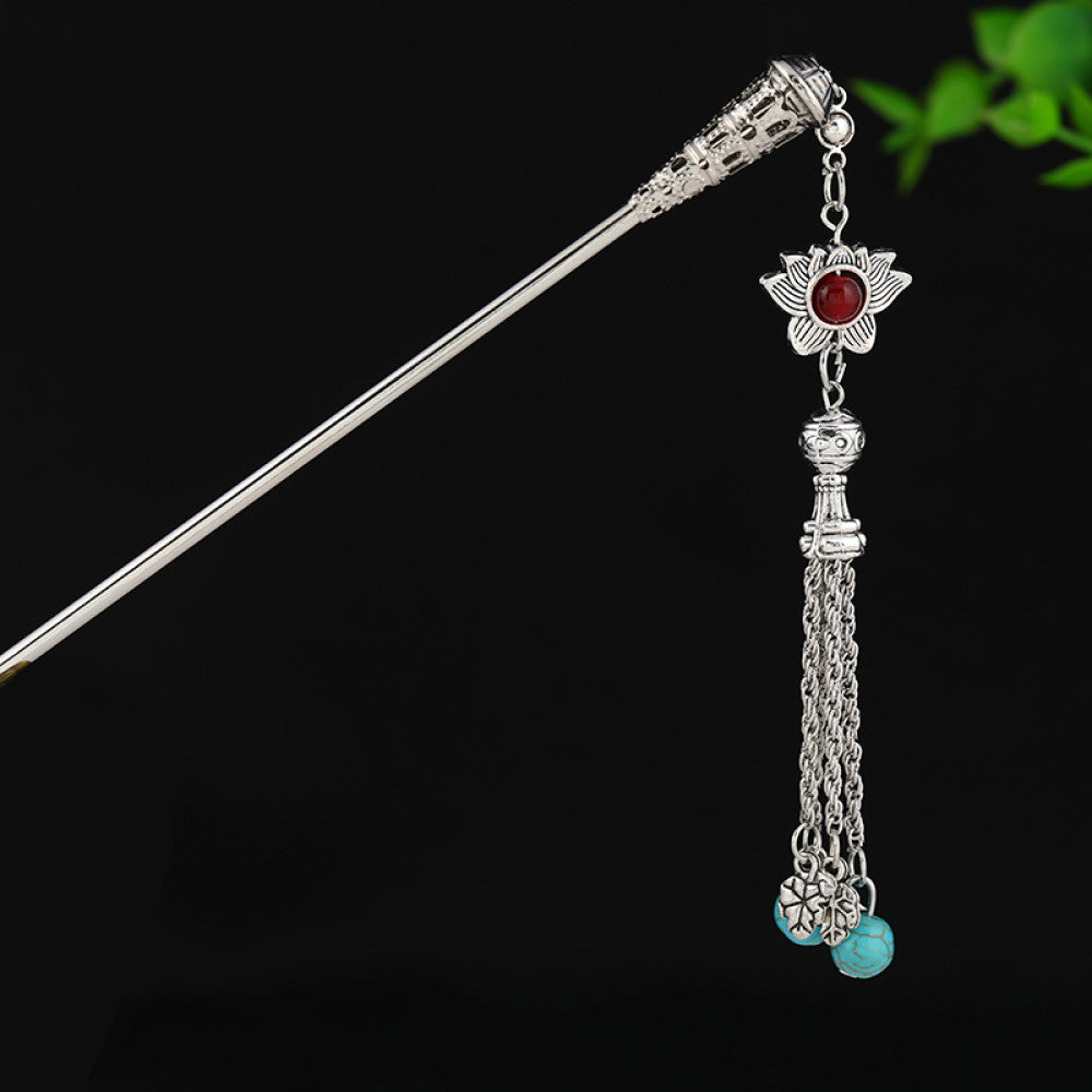 silver-tone hair stick featuring turquoise beads, an intricate round decorative element, and layered chain tassel fringe, displayed beside a white vessel green foliage  07